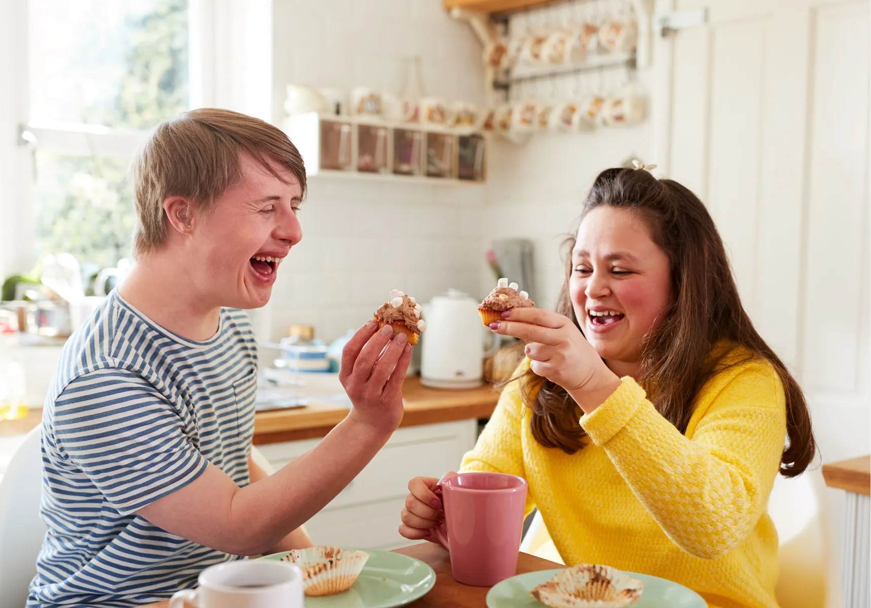 Two friends laughing together over morning tea at home